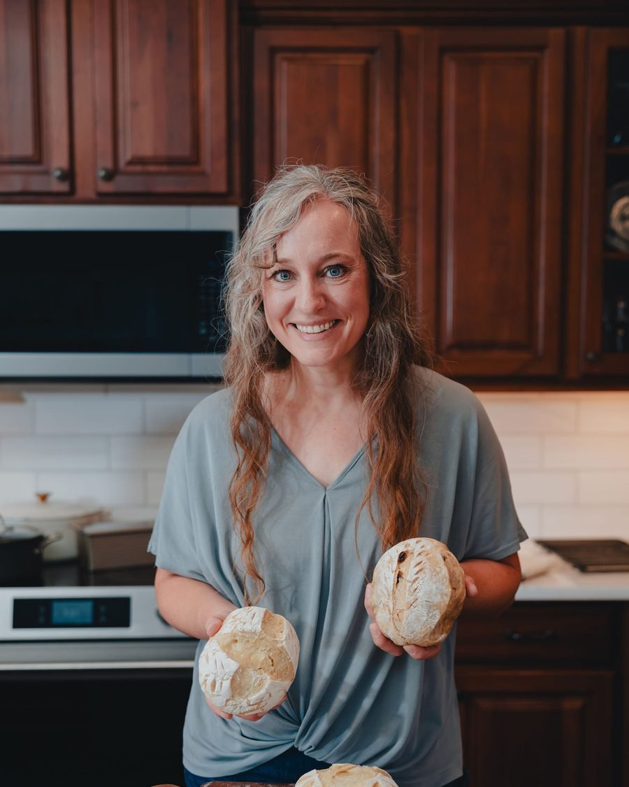 Rachel holding two fresh-baked sourdough boules in her kitchen
